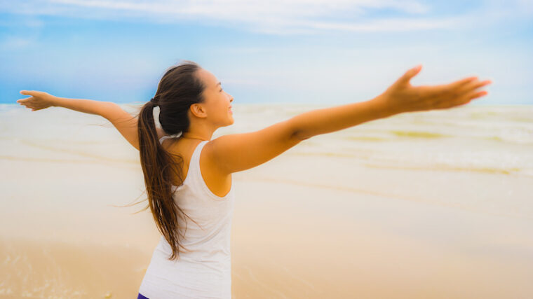 Kvinna med utsträckta armar på strand